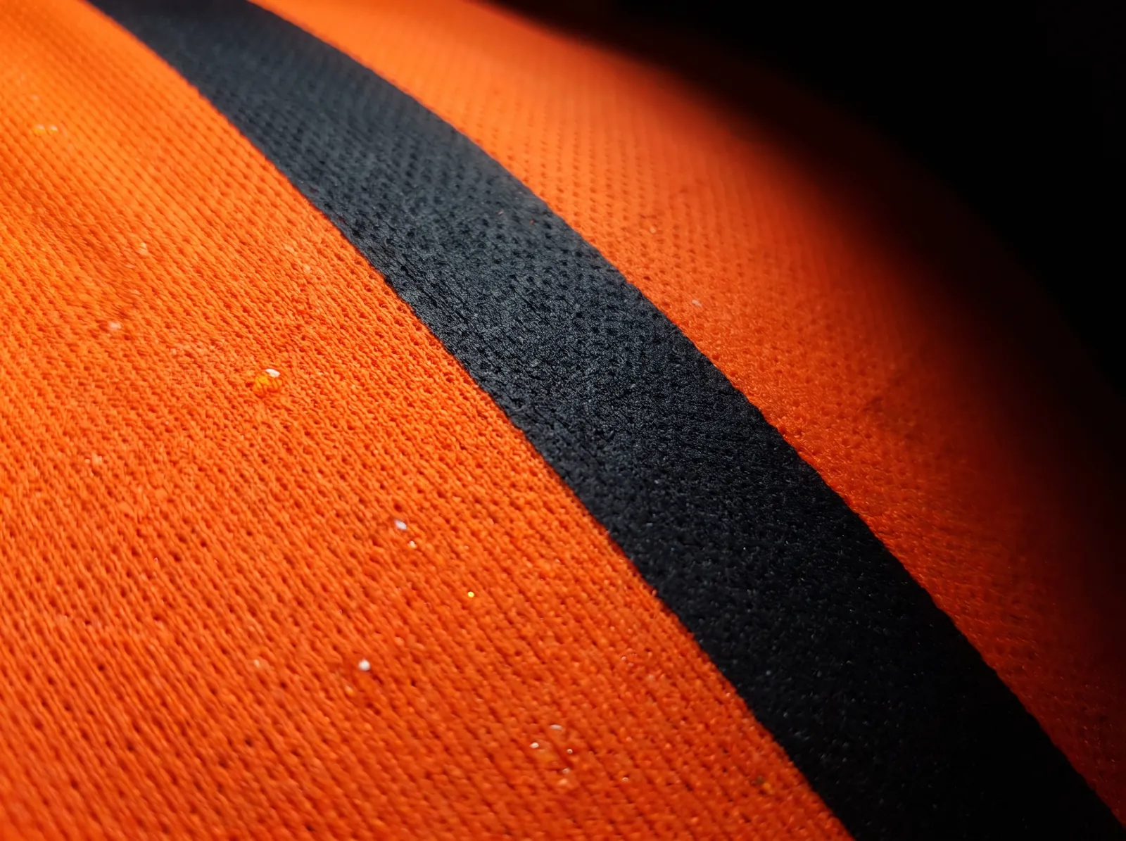Primer plano de tela dry fit naranja con franja negra sublimada dentro de la fibra